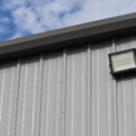 Gray metal building wall with a mounted exterior light against a blue sky.