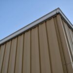Corner of a tan metal building against a clear blue sky.