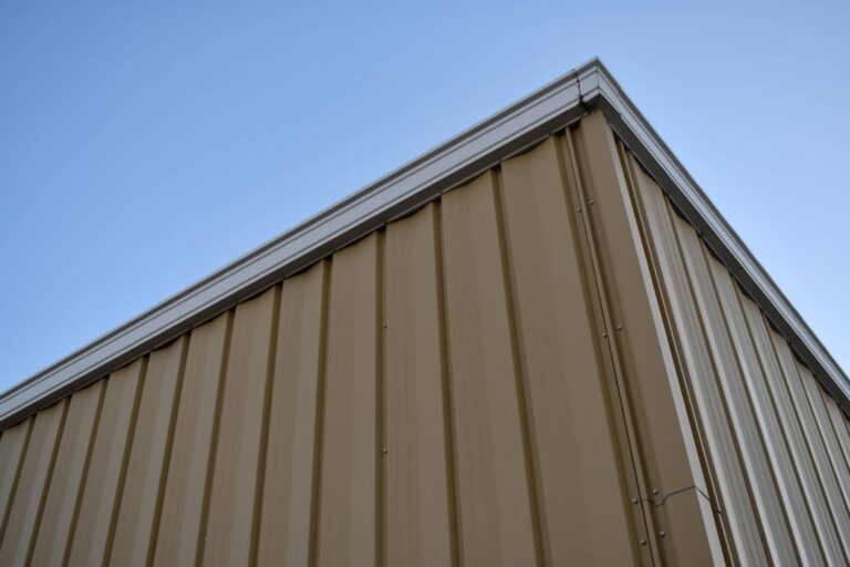 Corner of a tan metal building against a clear blue sky.