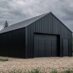 Black metal barn in a forest clearing under cloudy skies.